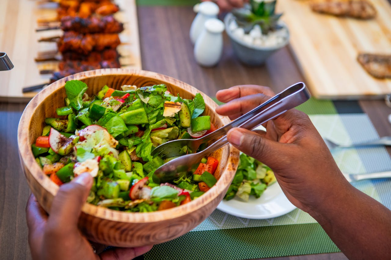 A vibrant, fresh salad in a wooden bowl served with grilled skewers on a table in Nairobi, Kenya.